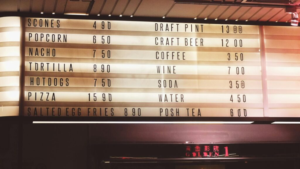 A brightly illuminated menu board showcasing various food and drink options with prices in a lively indoor setting.